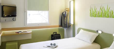 Una habitación de hotel con cama, escritorio con televisor, ventana y espejo adosado a la pared.