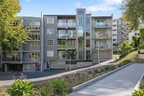 A multi-story residential building with balconies, a garage, and a paved driveway. - Comfortable city fringe Apt Near Basque Park (Eden Terrace)