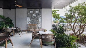 An outdoor seating area with tables and chairs, a stone wall, and potted plants. - The Leaf Boutique Hotel (Da Nang)