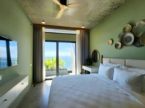 Un dormitorio con una cama grande, ventilador de techo, televisor, balcón con vistas y platos decorativos en la pared.