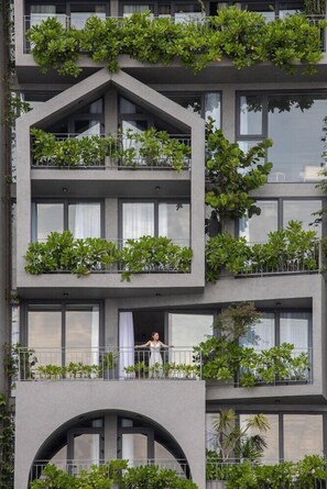 Un edificio de varios pisos con balcones cubiertos de vegetación, ventanas amplias y un arco central.