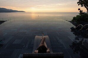Una persona descansando en una silla de descanso frente al mar, con vistas a un mar tranquilo y colinas lejanas.