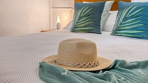 Una cama con un sombrero de paja, un plaid verde y dos almohadas con estampado de hojas.
