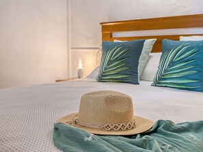 Ein Bett mit einem Strohhut, einer grünen Tagesdecke und zwei Kissen mit Blätermotiv.