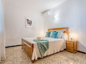 Ein Schlafzimmer mit einem hölzernen Bett, einem Nachttisch, einer Wand-Klimaanlage und einem Bilderrahmen mit einem Herbstblatt.