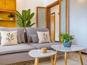 Ein modernes Wohnzimmer mit einem grauen Sofa, passenden Kissen, einem kleinen runden Tisch und einer Topfpflanze.