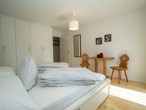A bedroom with a bed, a wardrobe, a table with chairs, and a mirror on the wall. - FURTÜNADA, (Scuol) by Interhome (Scuol)
