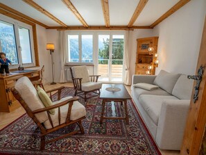 A cozy living room with a sofa, chairs, a coffee table, and a rug. There are large windows with a view of mountains. - FURTÜNADA, (Scuol) by Interhome (Scuol)