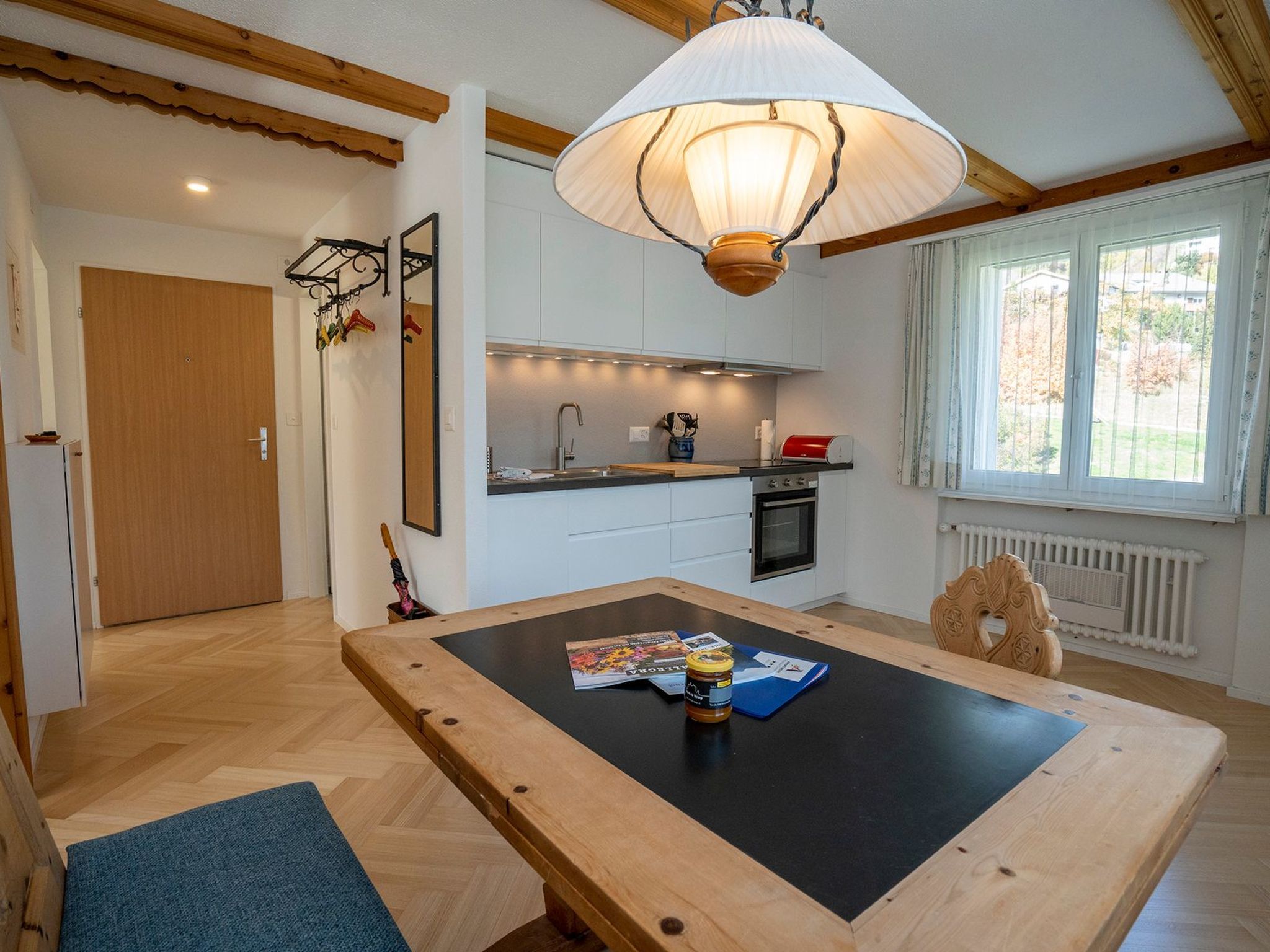 Une cuisine chaleureuse avec une table à manger, un luminaire suspendu et une fenêtre avec des rideaux.