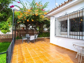 A patio with a tiled floor, a table with chairs, and a view of a garden with flowering plants. - Villa Francisca by Casasol by Interhome (Nerja)