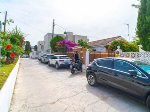 Une rue résidentielle bordée de voitures garées et une entrée fermée par un portail menant à une propriété.