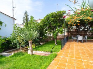 Une terrasse avec un sol carrelé, un petit jardin avec de la pelouse et un palmier, et une pergola ornée de fleurs.