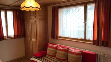 A cozy room with a wooden ceiling, a red sofa with striped cushions, and a window with curtains.