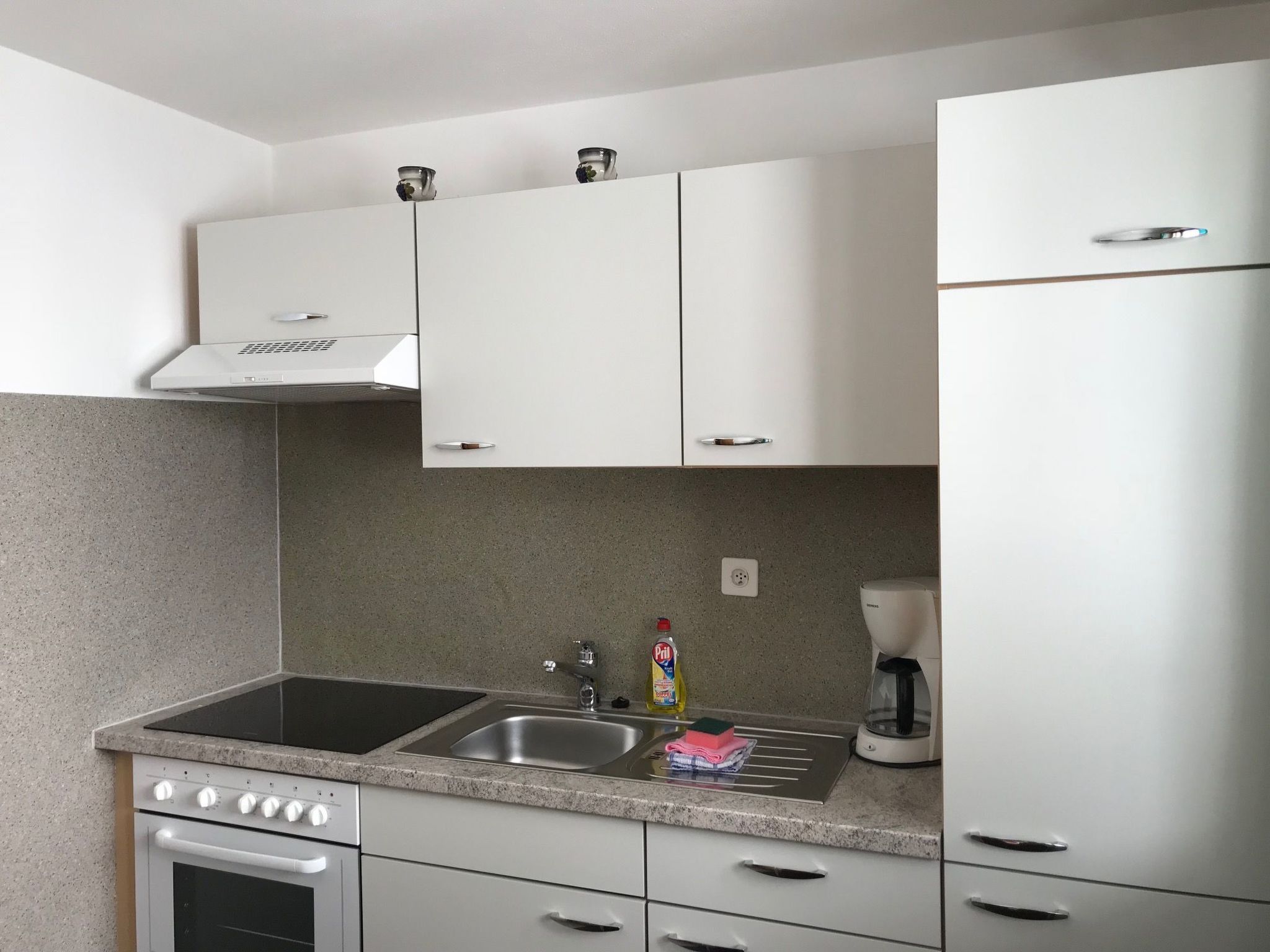 Una cocina moderna con armarios blancos, un lavamanos doble, una estufa y una cafetera.