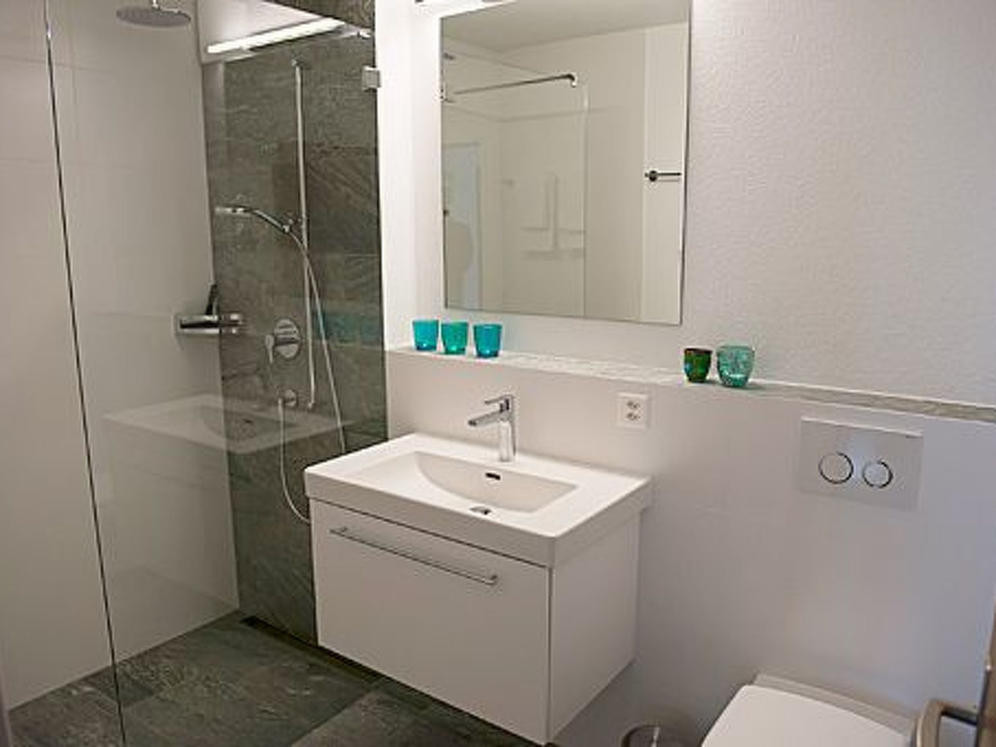 Een moderne badkamer met een glazen douchecabine, een wit wastafeltje en een spiegel erboven.