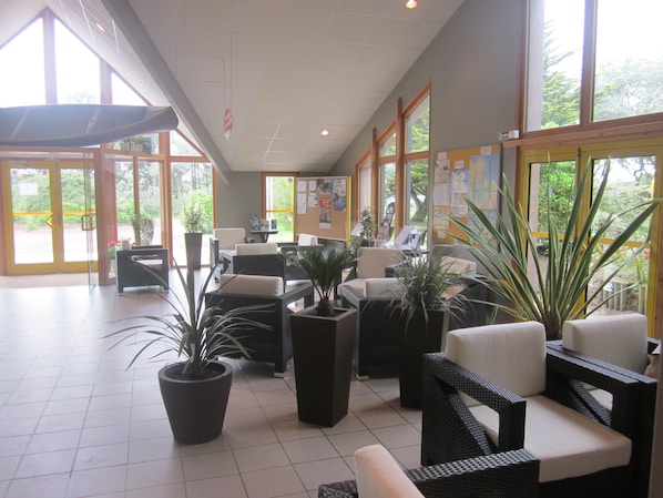 A spacious lobby with large windows, comfortable seating areas, and potted plants. - Vvf Villages Portbail (Port-Bail-sur-Mer)
