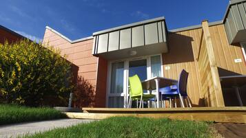 A modern building with a flat roof, large windows, and a small outdoor seating area with two chairs.