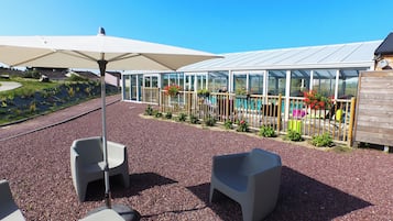 En terrasse med udendørs møbler, en swimmingpool og et drivhus.