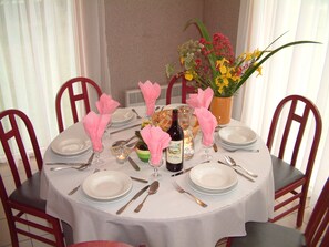 A round dining table set for four with white tablecloth, pink napkins, and a vase of flowers. - Vvf Villages Portbail (Port-Bail-sur-Mer)