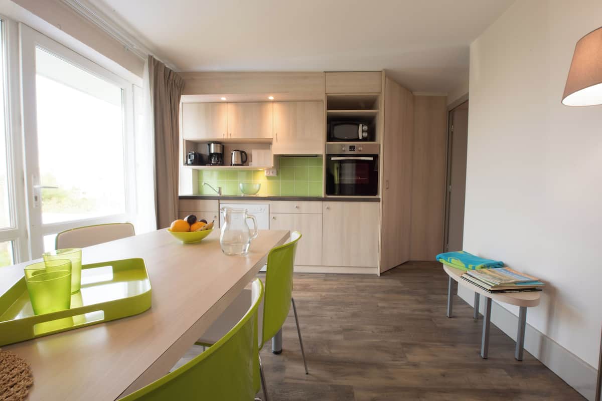 A modern kitchen with a dining area, including a table with chairs, a bench, and a window with curtains.