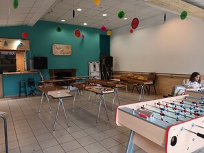 Una habitación con mesa de futbolín, una zona de cocina y un espacio de descanso con sofá.