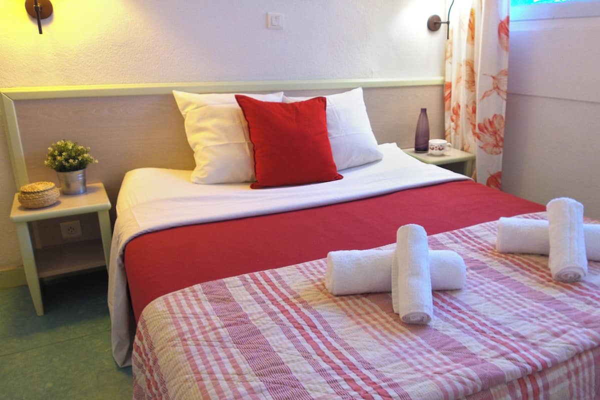 Ein Hotelzimmer mit Bett, Nachttisch, kleiner Topfpflanze und einem Fenster mit Vorhängen.