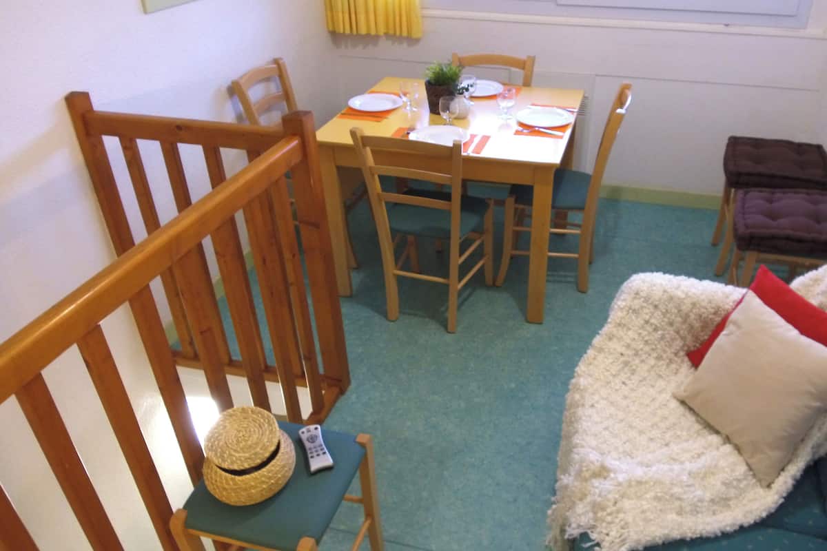 Ein Essbereich mit einem Tisch, gedeckt für vier Personen, umgeben von Holzstühlen. Auf einem Stuhl liegen ein Fernseher-Sender und ein Strohhut.