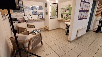 A room with wicker furniture, a small round table, a shelf with informational materials, and a radiator.
