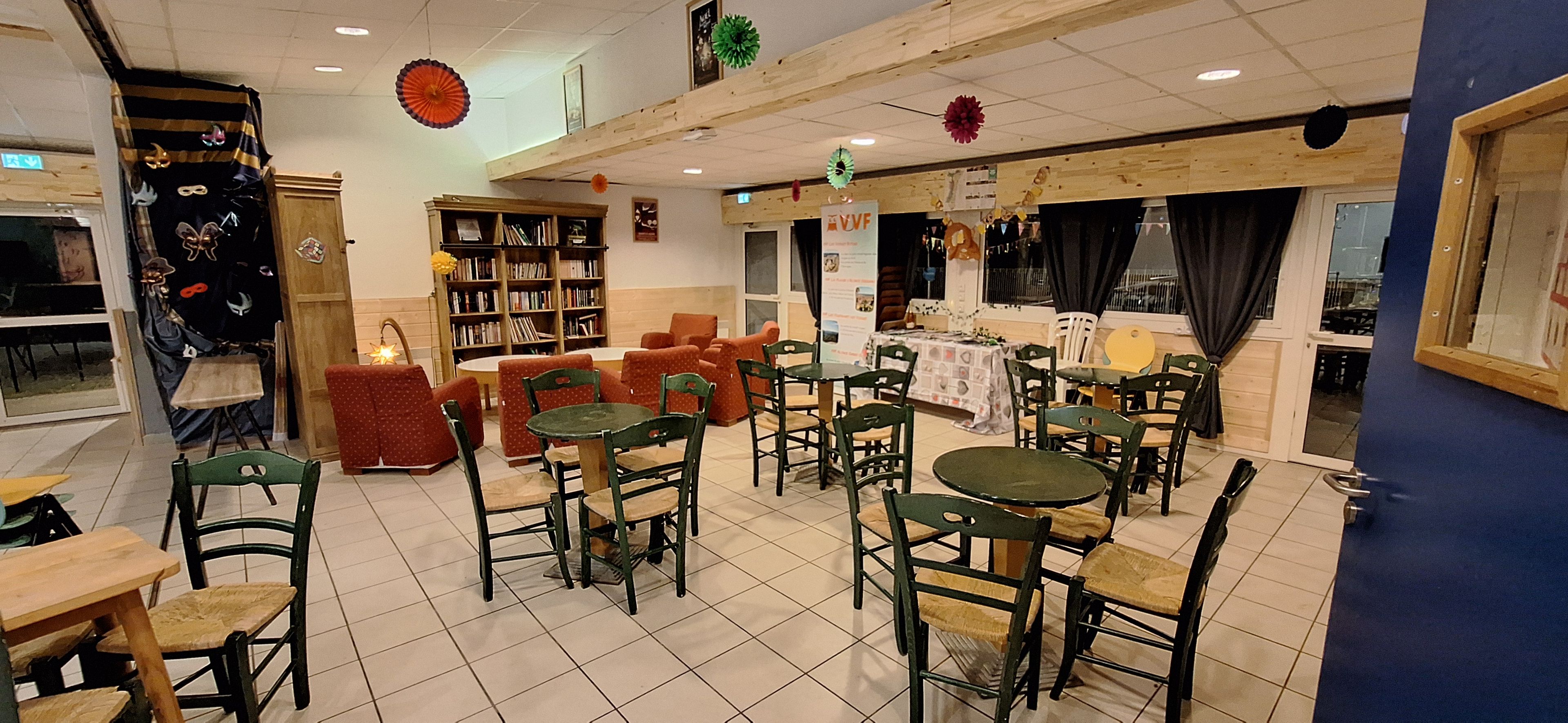 A restaurant with multiple tables and chairs, a bookshelf, and a window with curtains.