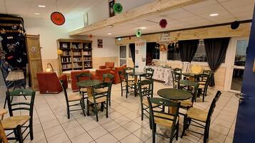 A restaurant with multiple tables and chairs, a bookshelf, and a window with curtains.