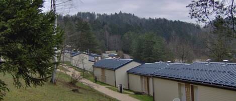 A row of single-story cabins with a dirt path leading to them, surrounded by trees and a forested hill in the background.
