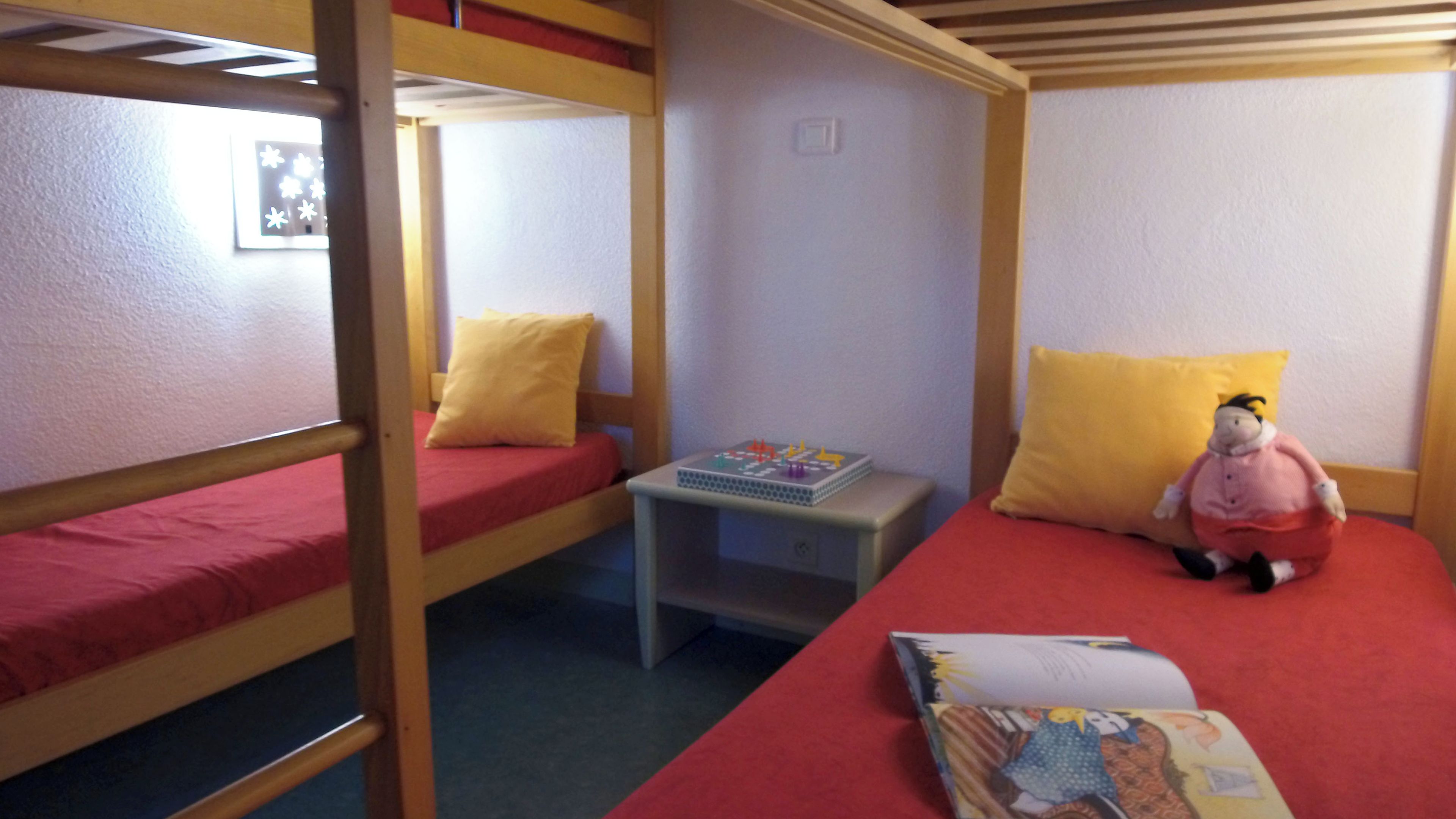 Habitación con literas, una pequeña mesa, un juguete y un libro.
