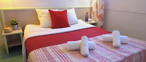 Een hotelkamer met een bed, nachtkastje, kleine potplant en raam met gordijnen.