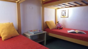 A room with two single beds, a small table with a board game, a stuffed toy, and a wall-mounted light fixture.