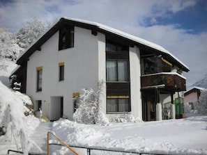 Ein zweigeschossiges Gebäude mit geneigtem Dach, großen Fenstern und einer schneebedeckten Fassade.