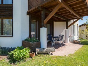 A covered outdoor seating area with a table and chairs, a planter with flowers, and a stone feature. - Chasa Bainvgnü, (Scuol) by Interhome (Scuol)