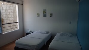 Ein Zimmer mit zwei Betten, einem Fenster, einem Nachttisch und Wandbildern.