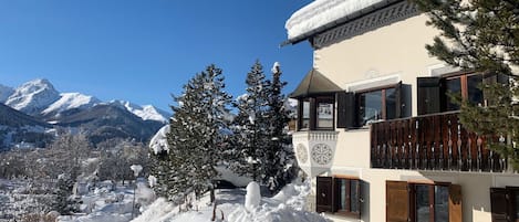Paisagem nevada de montanhas com um edifício com varandas e telhado coberto de neve.