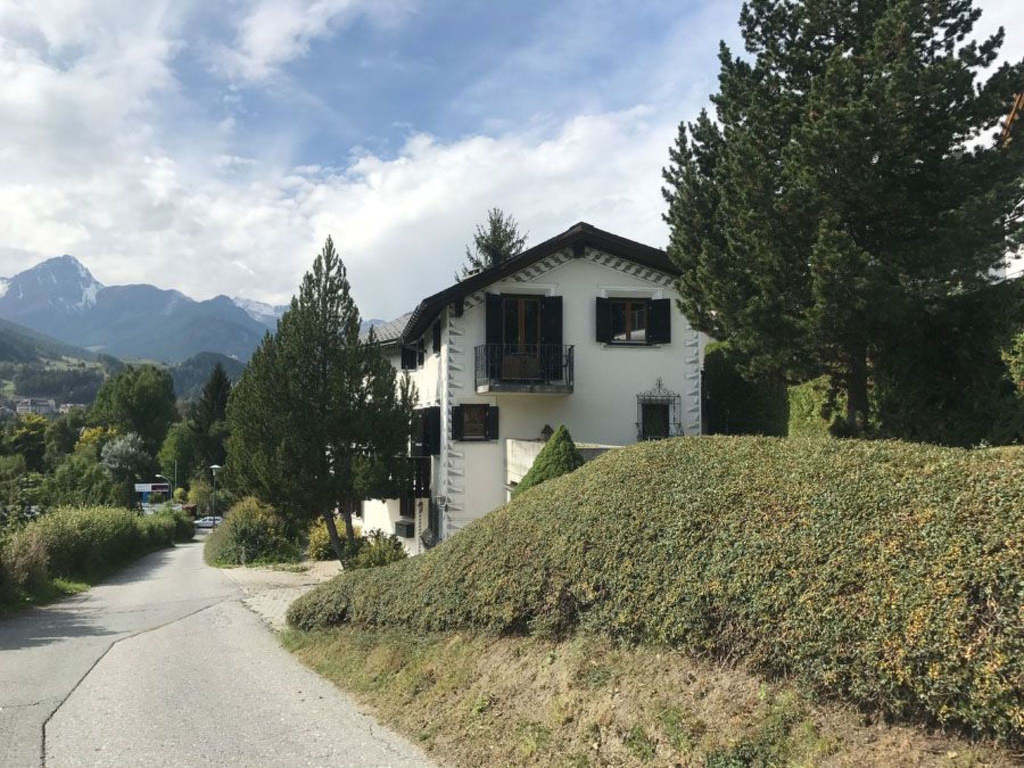 A two-story house with a balcony, surrounded by trees and a mountain backdrop.