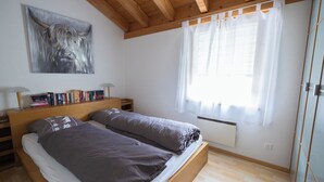Ein Schlafzimmer mit einem hölzernen Bett, einem Nachttisch, einer Lampe, einem Fenster mit Vorhängen und einem Bild an der Wand.