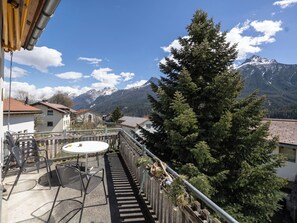 A balcony with a table and chairs, overlooking a mountain landscape with a large evergreen tree and a building with a red roof. - Senda 517c, (Scuol) by Interhome (Scuol)