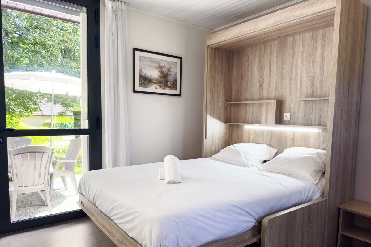 Um quarto com uma cama, uma mesinha de cabeceira, uma cadeira e uma janela com cortinas.