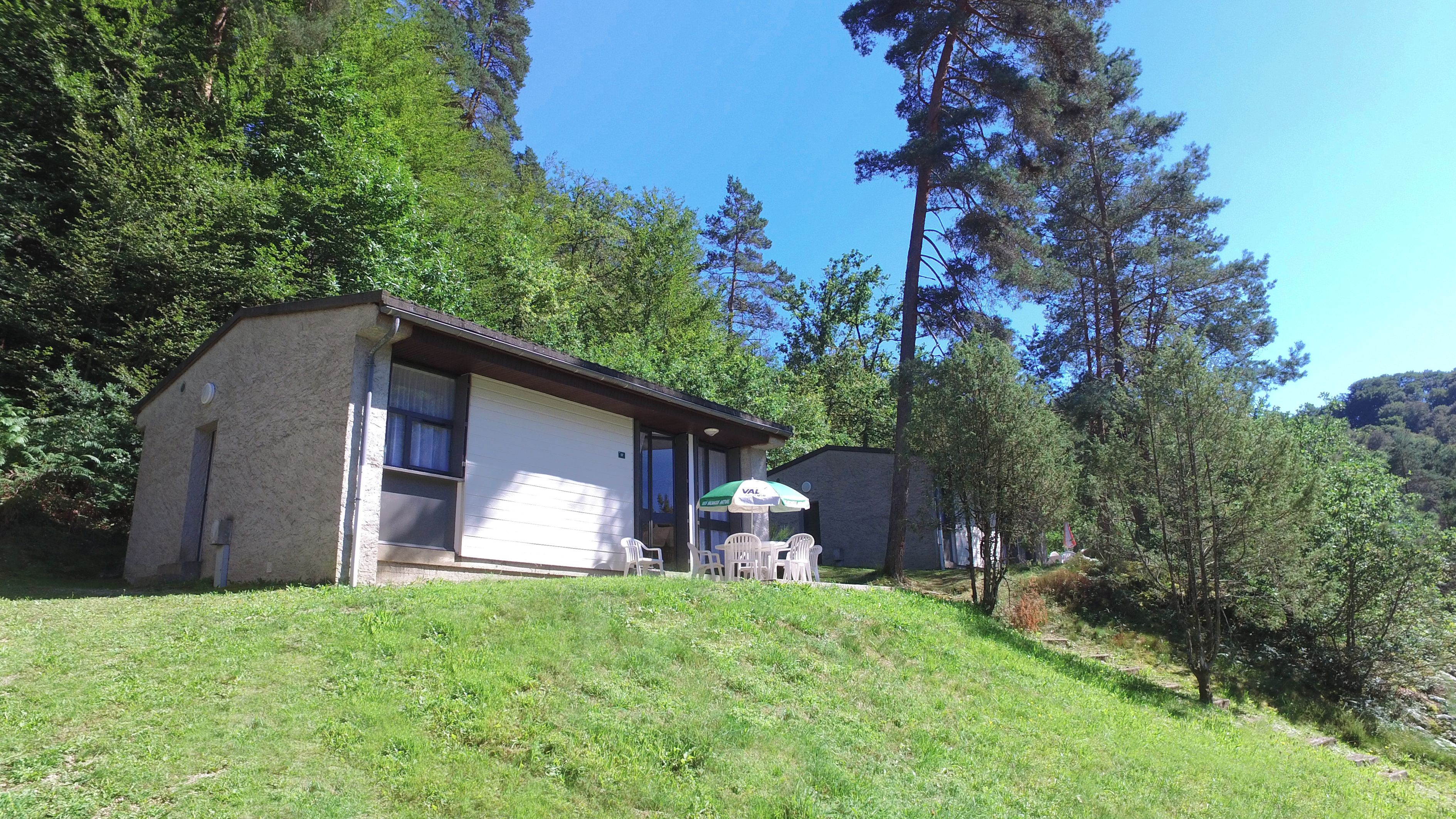 Una casita con un patio, rodeada de árboles y una colina cubierta de césped.