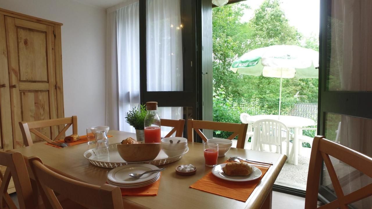 Una mesa de comedor con alimentos para el desayuno, sillas, una ventana que da a zonas verdes y una puerta.