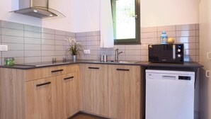 A kitchen with wooden cabinets, a dishwasher, a microwave, and a window above the sink. - Vvf Villages Champs Sur Tarentaine (Champs-sur-Tarentaine-Marchal)