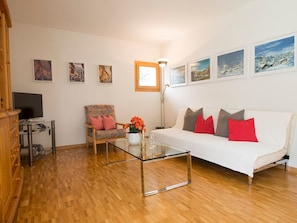 A living room with a sofa, armchairs, a coffee table, and a TV. There are framed pictures on the wall and a window with a view. - Haus Betschart, (Scuol) by Interhome (Scuol)