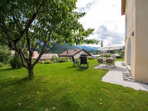 A well-maintained garden with a lawn, a tree, outdoor furniture, and a view of a mountain and a church in the background. - Haus Betschart, (Scuol) by Interhome (Scuol)