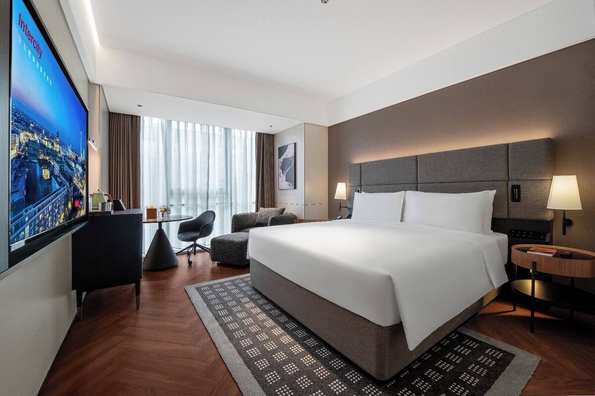 Une chambre d’hôtel avec un grand lit, un bureau, une chaise, une télévision et une vue sur la ville.