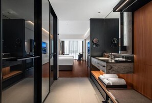 Une chambre d’hôtel moderne dotée d’un grand lit, d’un coin salon, d’une salle de bain avec un meuble-lavabo et d’un grand miroir.