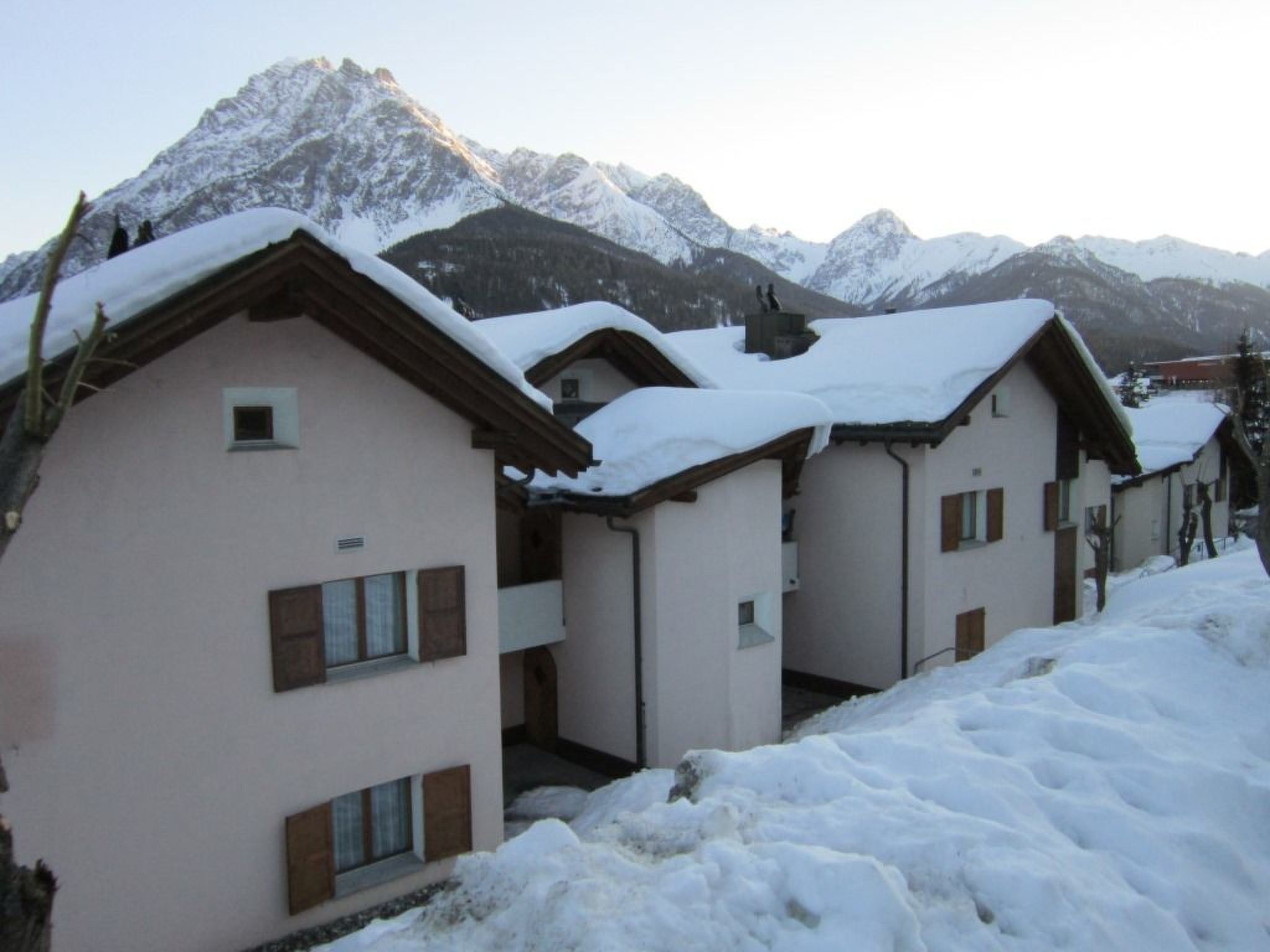 Une rangée de bâtiments de style chalet, aux toits couverts de neige, se dressant sur fond de montagnes enneigées.